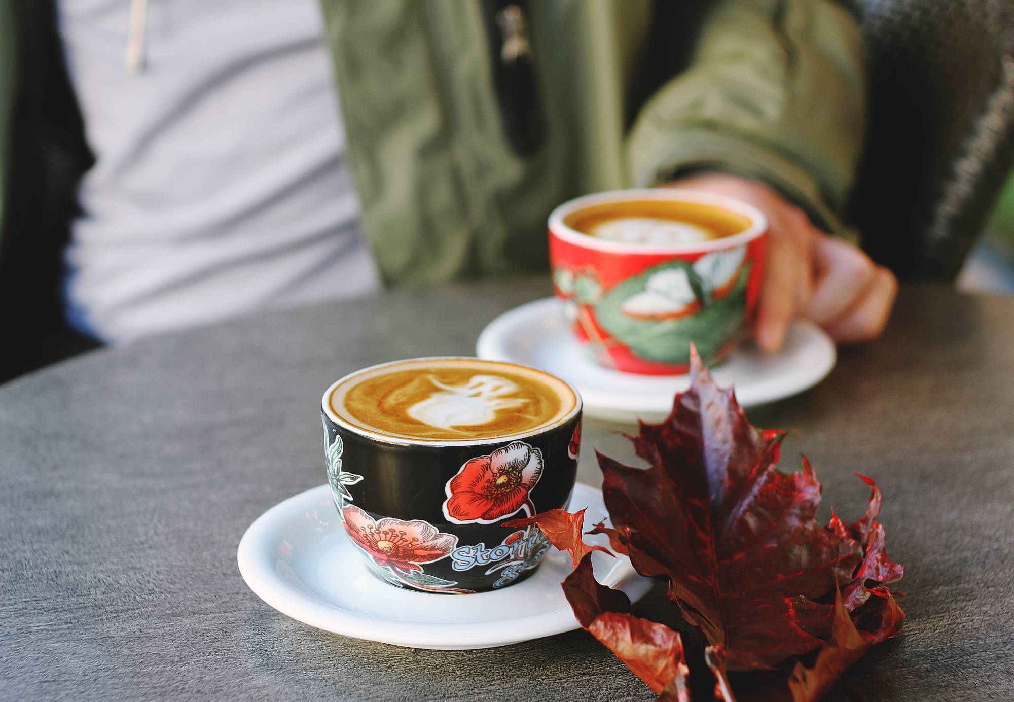 Two lattes with ghost latte art, and a red fall leaf sitting on a table.