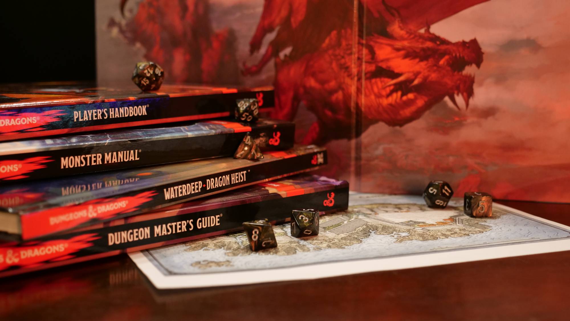 Dice resting on a stack of Dungeons and Dragons sourcebooks including the Players Handbook, the Monster Manual, Waterdeep - Dragon Heist, and the Dungeon Master's Guide. Under the stack is a map of Candlekeep, and in the background is a Dungeons and Dragons 5e DM screen.