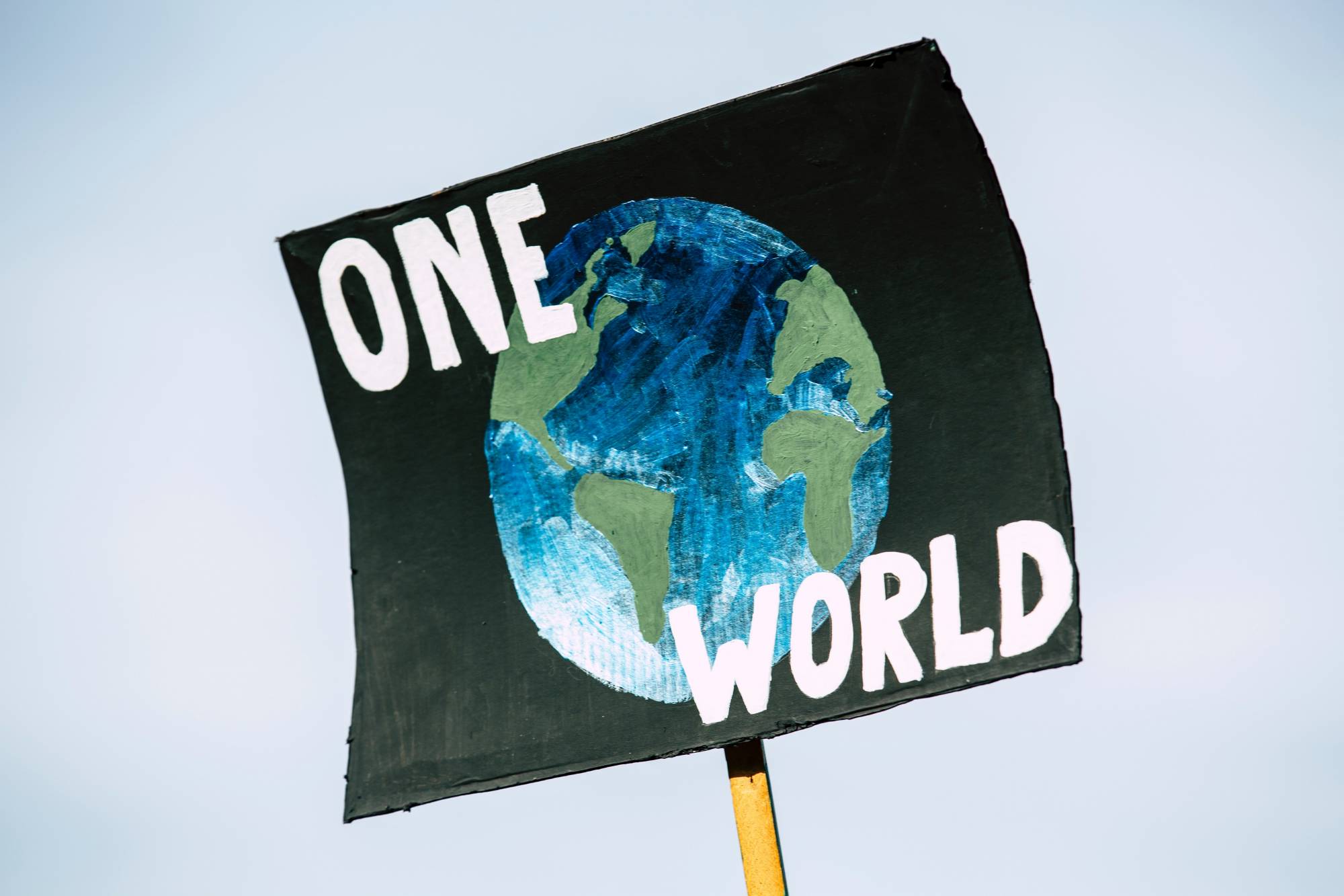 A black poster against a blue sky with a blue and green painting of earth. Over the painting is white text that reads "One World"