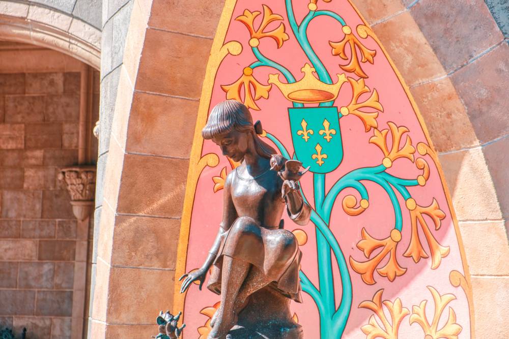 A sculpture of the Disney princess Cinderella. Background is a pink, green and yellow castle wall.