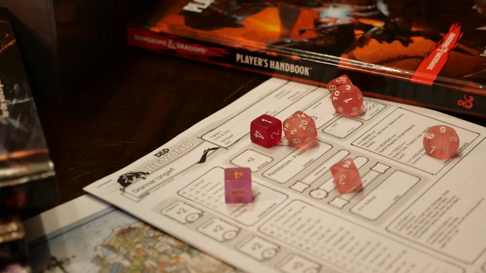 Pink and red dice resting on a character sheet next to a Dungeons and Dragons Player's Handbook.