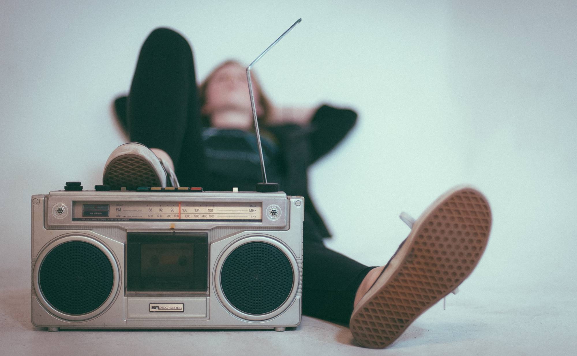 Person reclining against a wall with their foot on a boombox