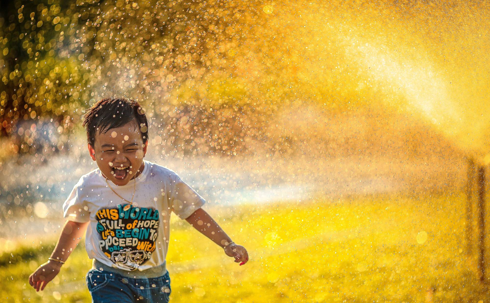 Photo of a small boy running past a water sprinkler