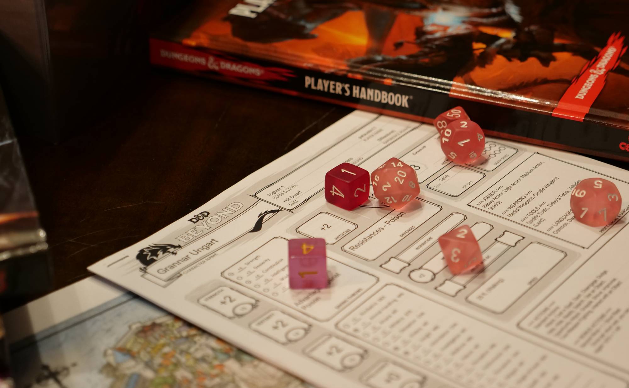 Pink and red dice resting on a character sheet next to a Dungeons and Dragons Player's Handbook.