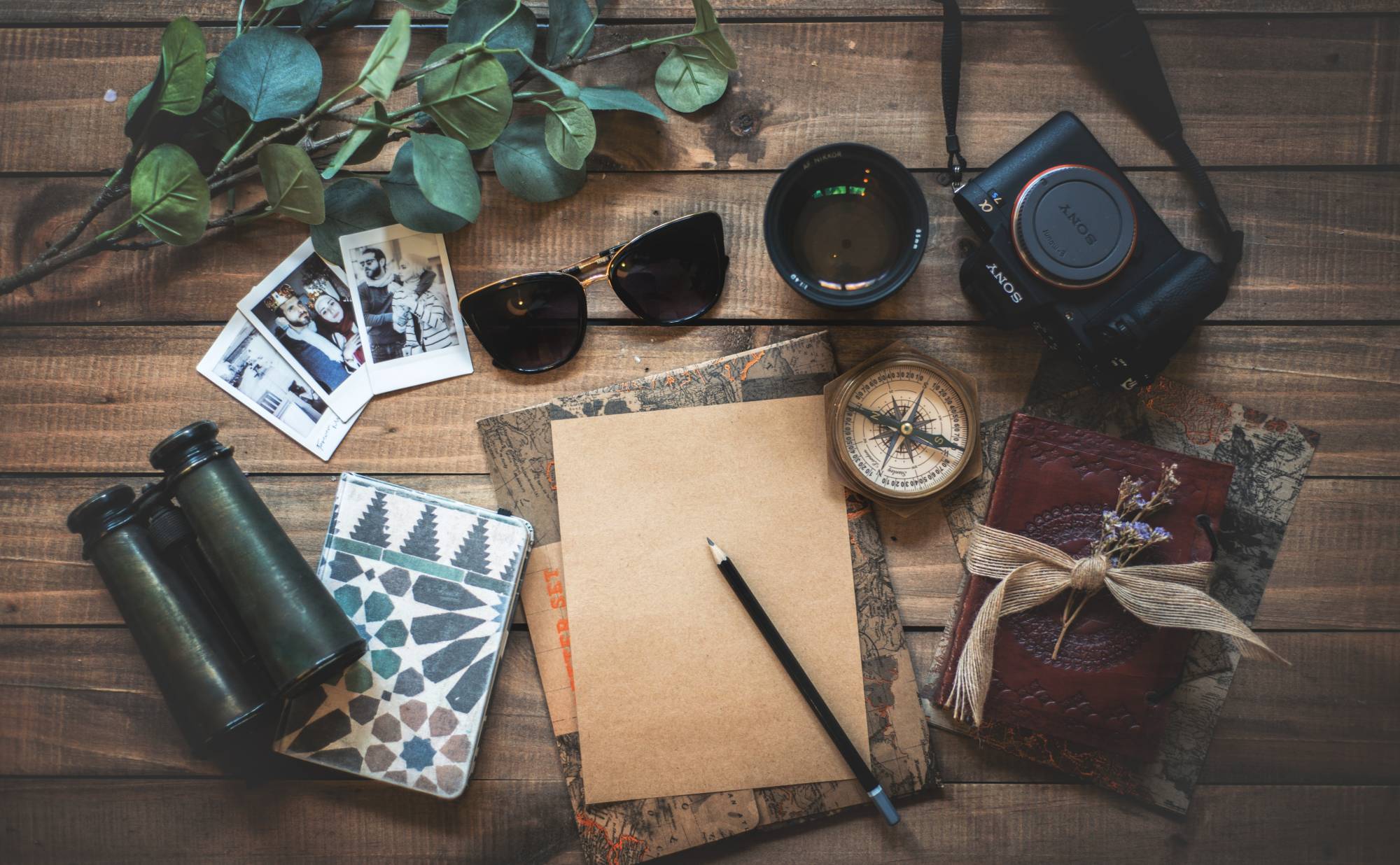 Compass, sunglasses, camera, binoculars, leaves, cards, and journals on a desk
