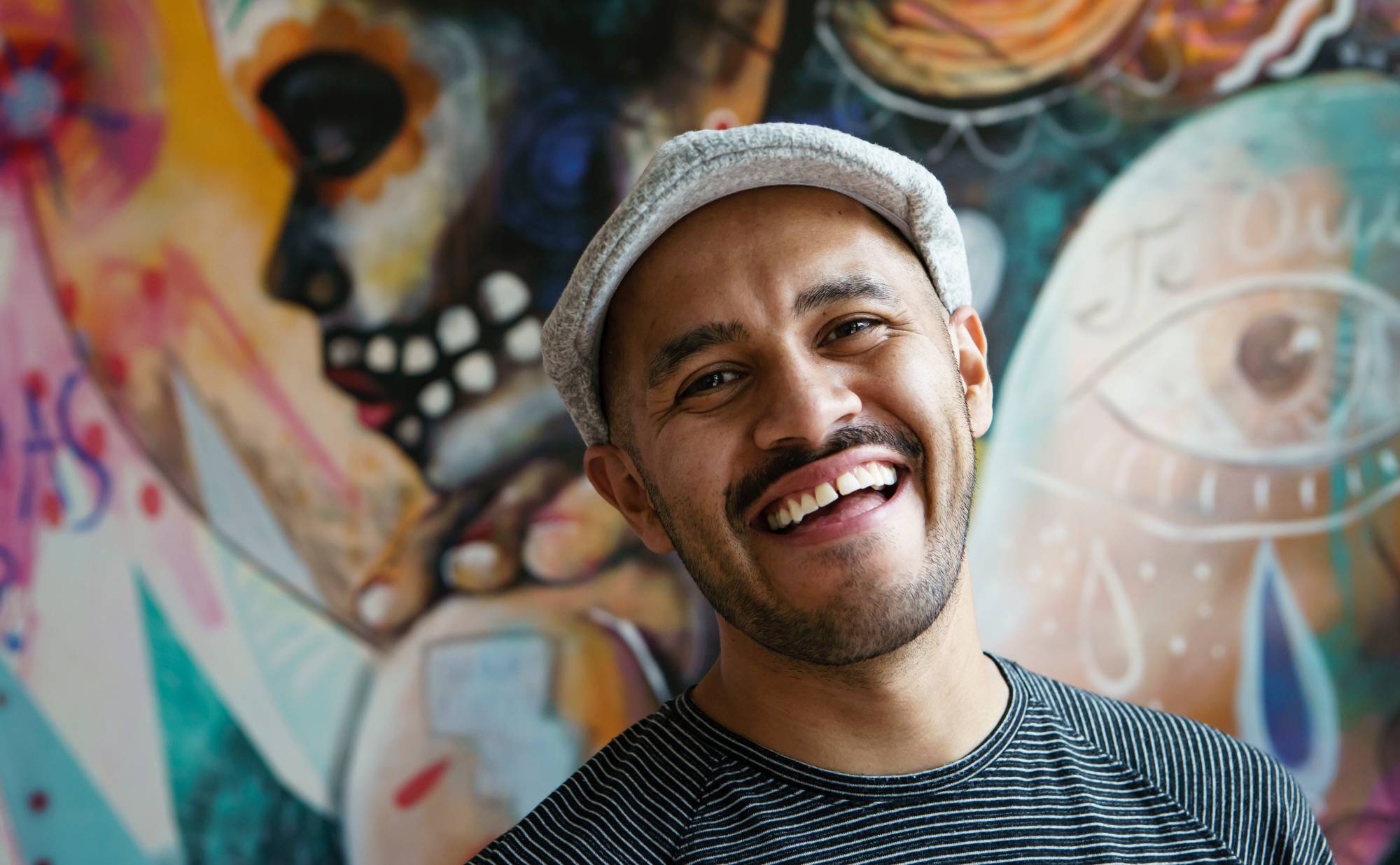 A photo of muralist and performer Armando Silva. Background is a colorful mural.