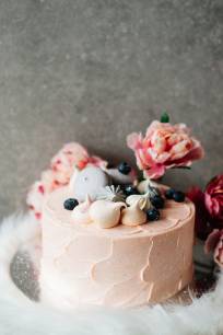 Pink cake with meringue kisses on top, flowers in background