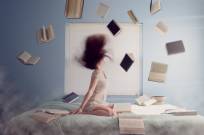 Photo of a woman in bed surrounded by books