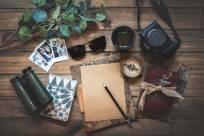 Compass, sunglasses, camera, binoculars, leaves, cards, and journals on a desk