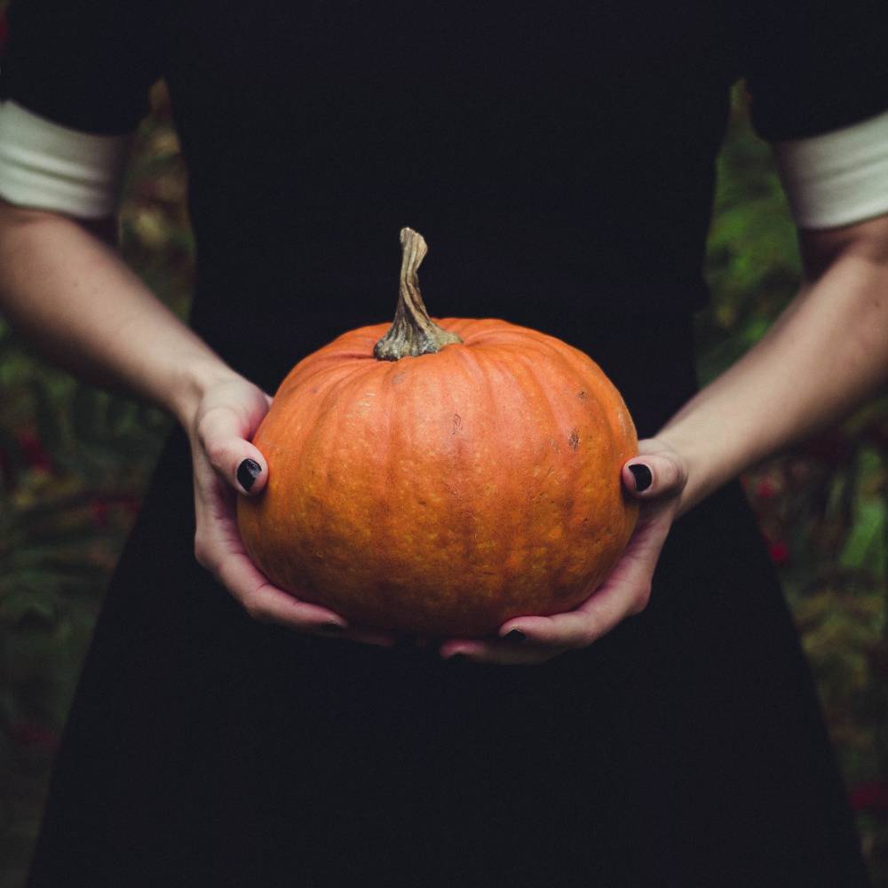 A person wearing a black dress holds an orange pumpkin