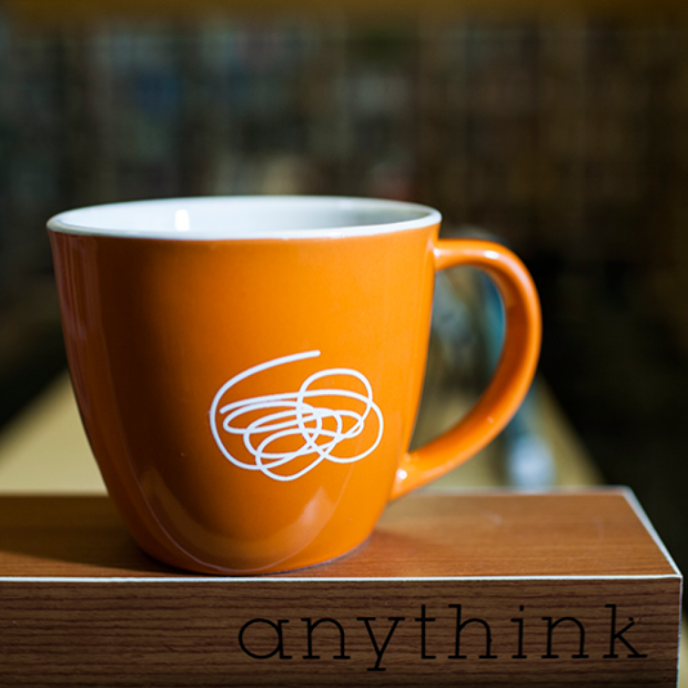 A orange mug with white Anythink doodle.
